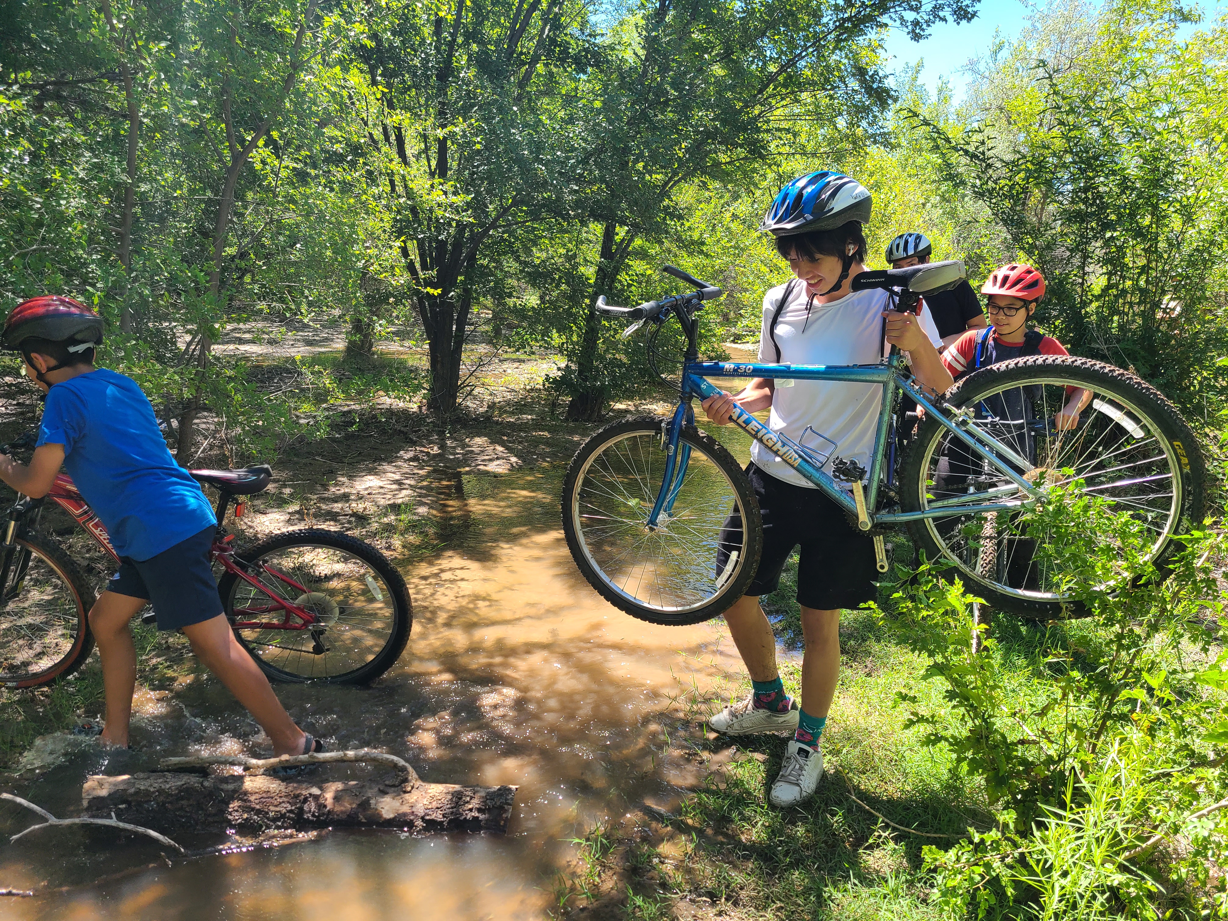 Two young people cross a creek while holding bikes